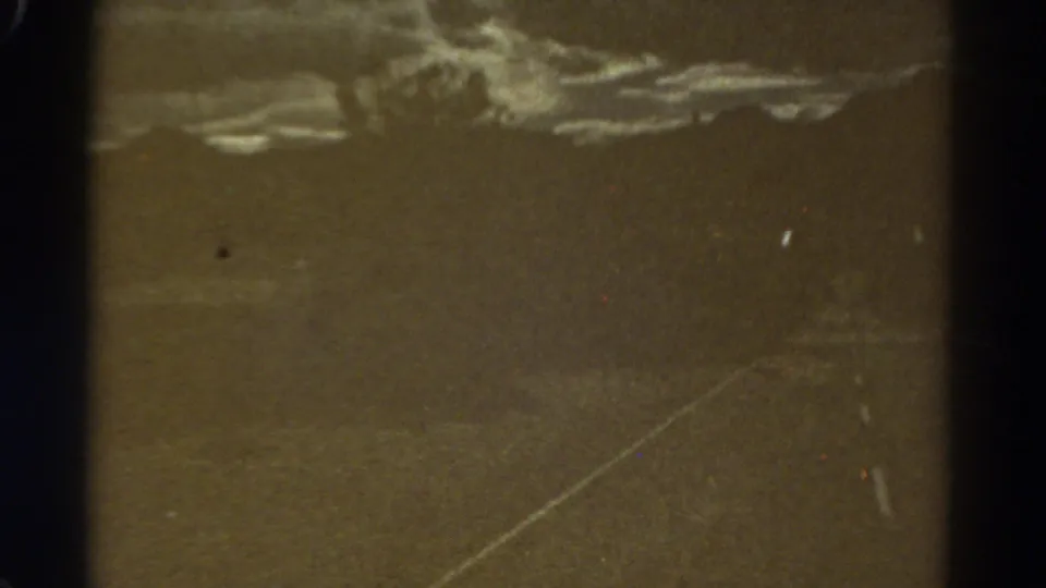 Muted 8mm frame from a 1967 Colorado road view, showing empty pavement, distant terrain, cloud cover and film abrasion.