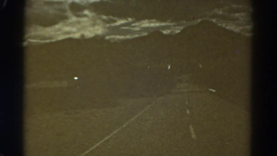 Final 1967 Colorado 8mm frame showing an empty road, low hills, cloudy sky, grain, dust and dark film gate edges.