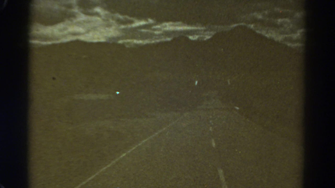 Dim road and cloudy horizon with a bright speck and film scratches.