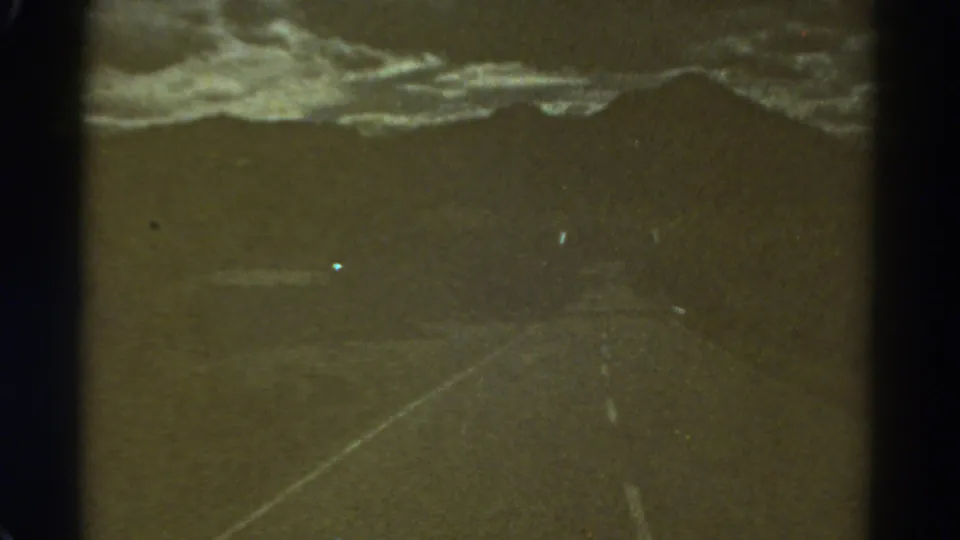 1967 Colorado home-movie frame of a dark road under a stormy sky, with light artifacts and vertical film borders.