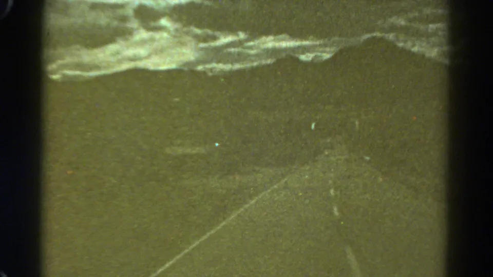 1967 Colorado 8mm frame with a faint road line, heavy grain, storm clouds, and soft low-light exposure.