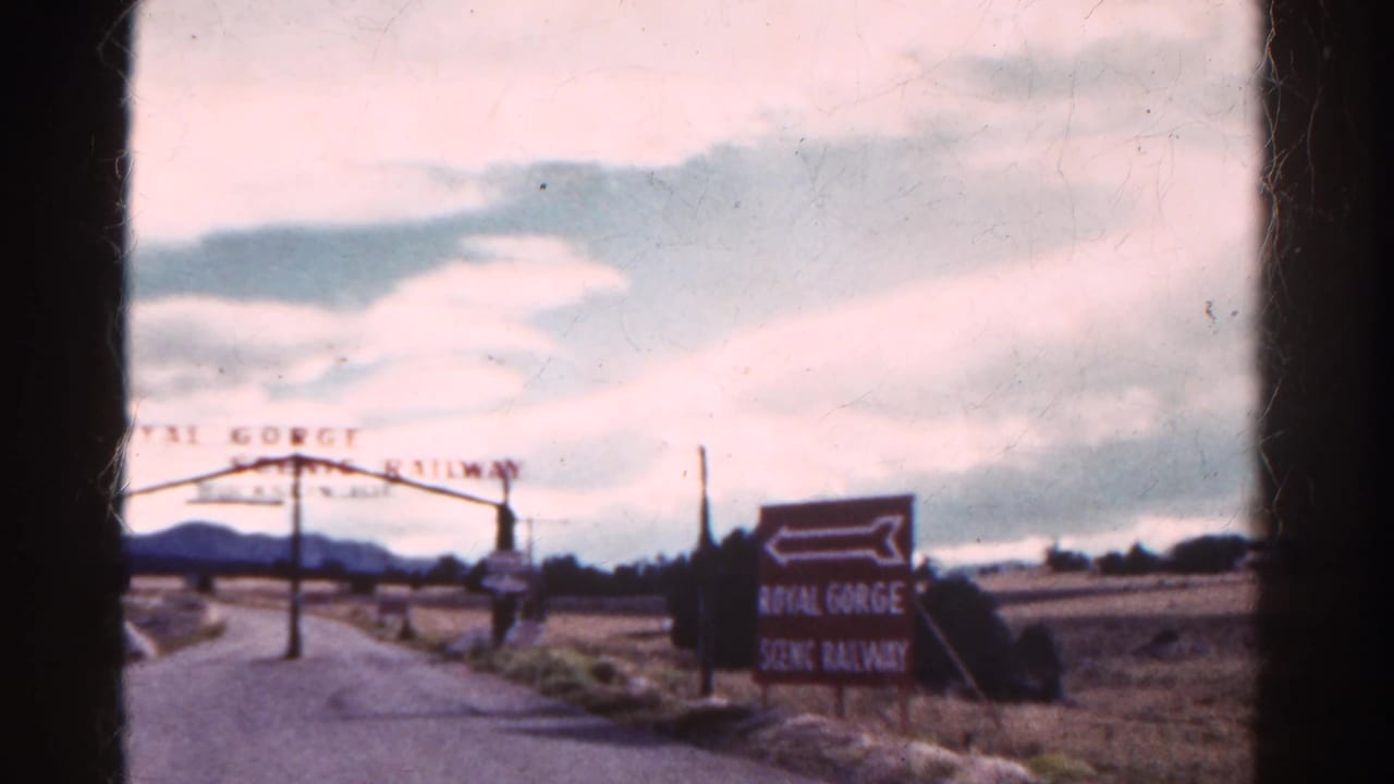 Roadside entrance arch for Royal Gorge Scenic Railway with a directional sign beside an open field.