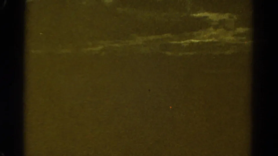 End-of-shot 8mm frame showing a dim greenish field of exposure, faint cloud texture, grain, and frame-edge shadow.