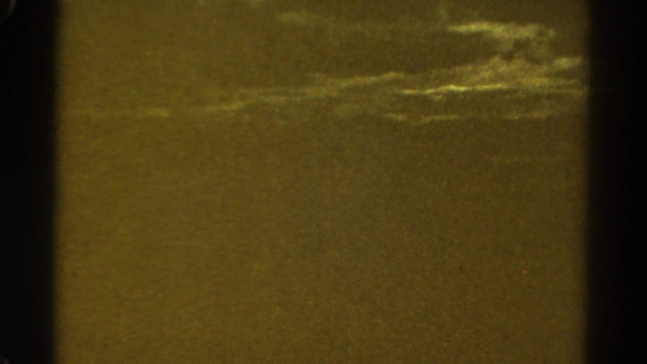 1967 8mm frame from Colorado metadata showing an indistinct dark surface, heavy grain, vertical gate edges, and faint bright streaks.