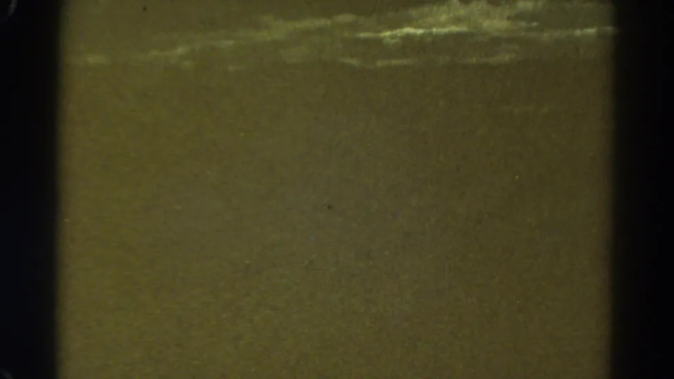 Soft 8mm frame with green-brown tint, heavy grain, dark film edge, and faint horizontal highlights on an indistinct outdoor surface.