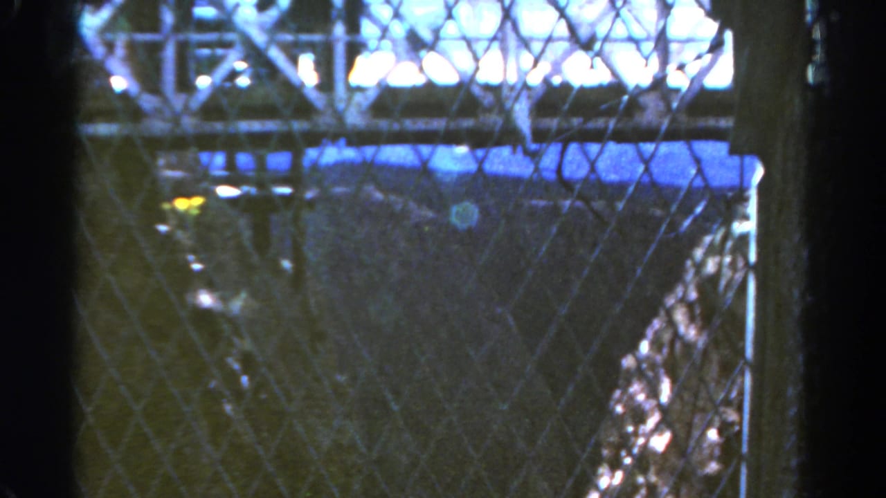 View through chain-link fence toward a dark shaft with bright light along the top edge.