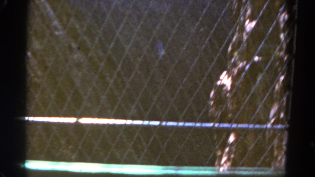 Wire fence and dark post beside a steep rocky drop or slope in low exposure.