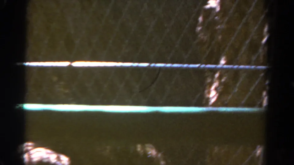 1967 8mm Colorado frame with chain-link fencing, dark terrain, and bright horizontal light streaks across the view.