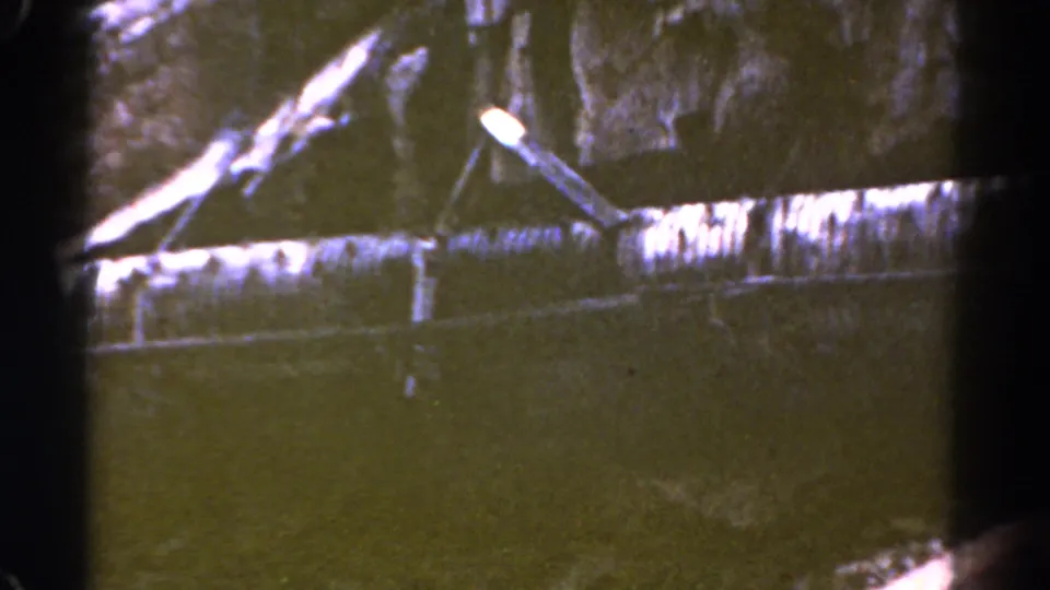 1967 Colorado 8mm frame showing a slanted utility lamp, stained ledge or wall, and dark water or shadowed ground in an industrial area.
