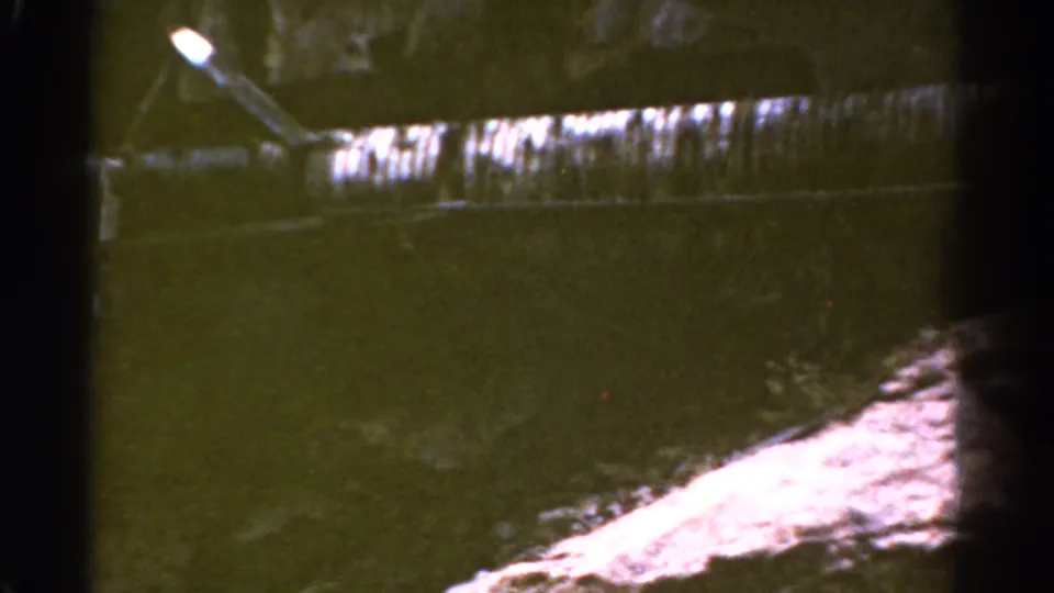 1967 Colorado 8mm frame with a stained industrial ledge, angled lamp, dark water or shadow, and pale ground at the lower right.