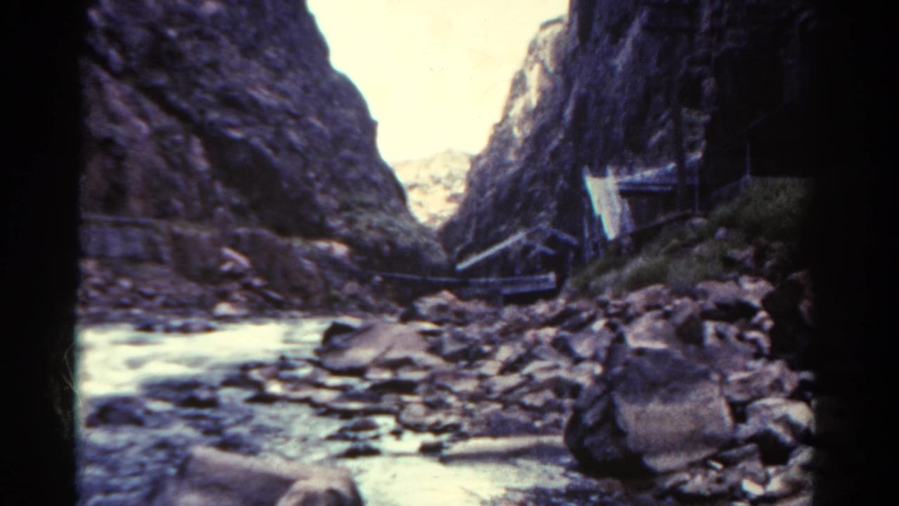 Canyon riverbed with rocks and a structure along the cliffside.