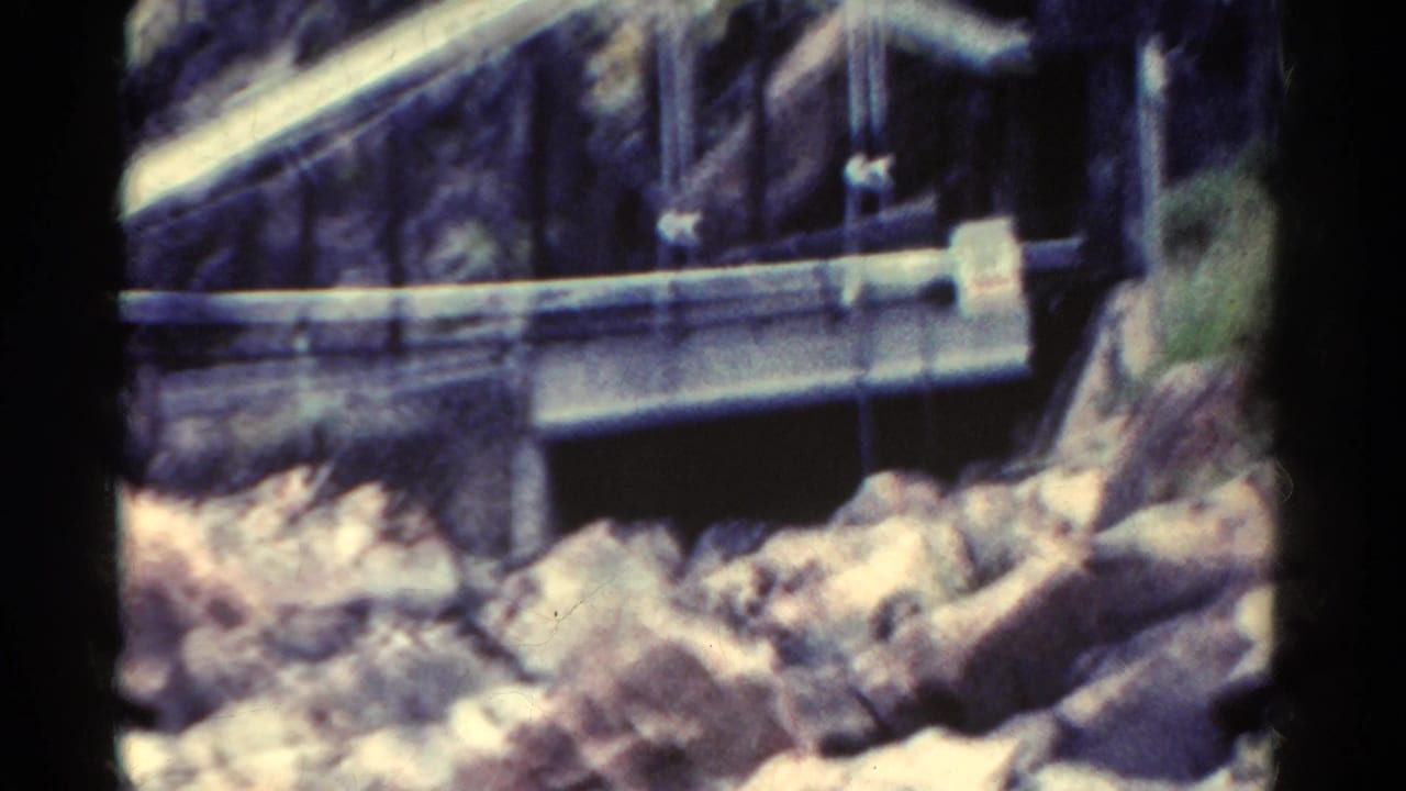 Closer view of a metal structure over rocks at the base of a steep canyon wall.