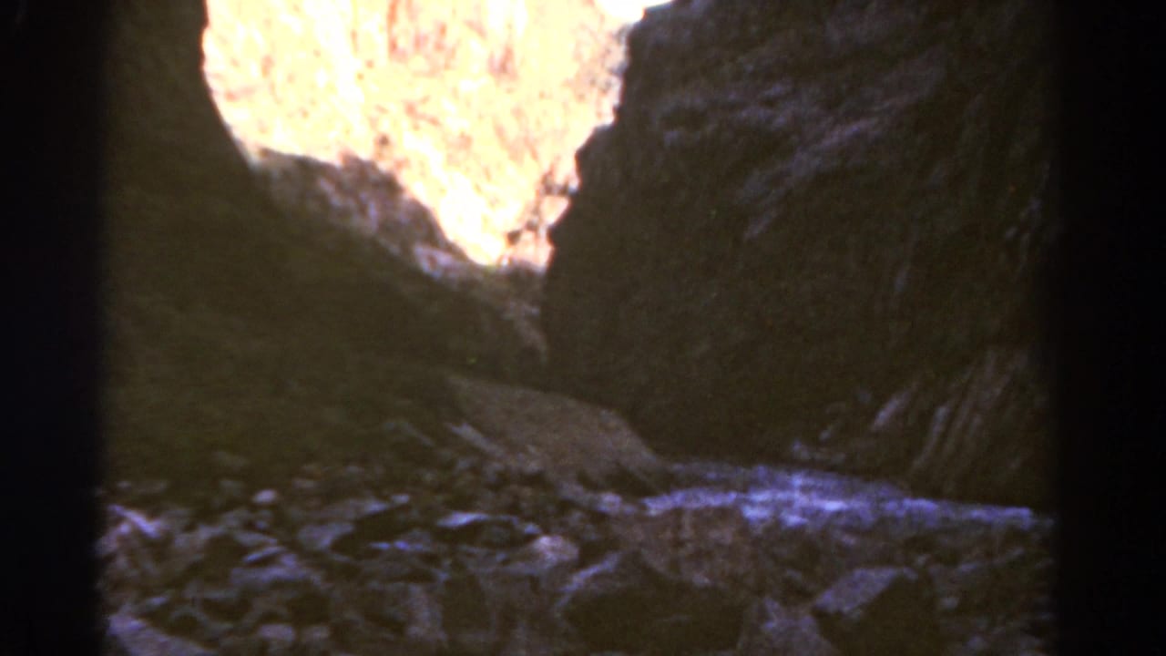 Dark canyon walls frame a bright sunlit opening above rocky ground.