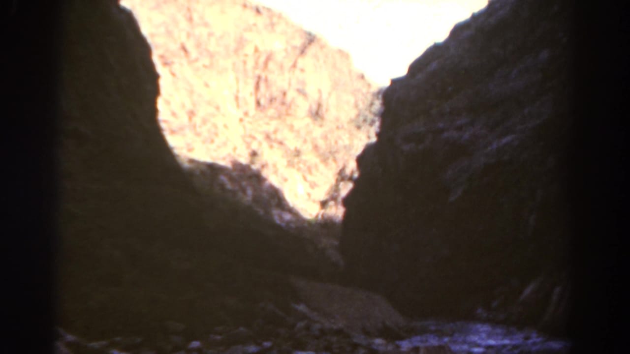 Rocky canyon walls and a bright opening are seen from inside deep shade.