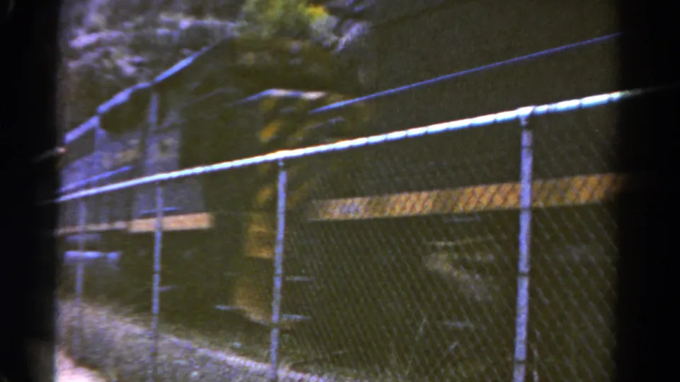 1967 Colorado home-movie frame showing fencing, canyon rock, and a fast dark train beside the track area.