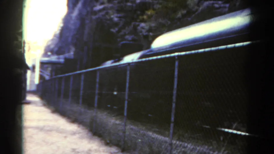 1967 Colorado 8mm frame showing the upper portion of a rail car moving behind fencing in a rocky corridor.