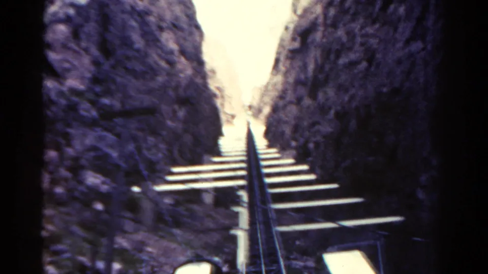 Passenger-perspective 8mm frame of a steep Colorado mountain railway running upward through dark canyon walls.