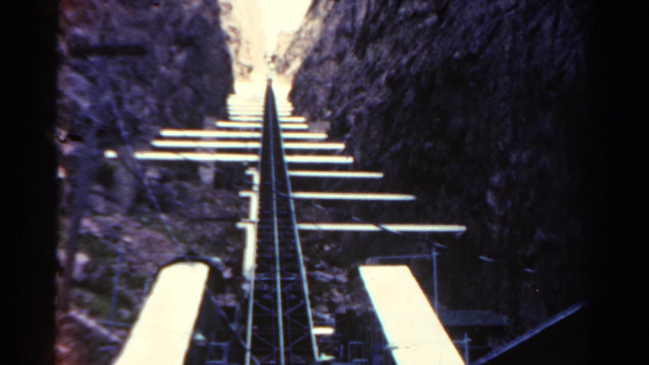 Roller coaster track rises between dark rocky walls toward a bright opening.