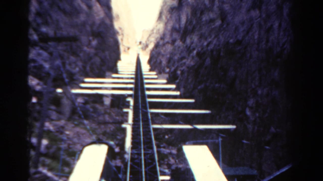 Ascending roller coaster rails and cross ties continue through a rocky corridor.