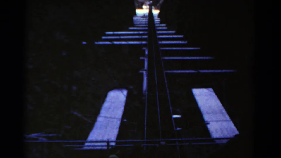 Shadowed 8mm frame of the roller coaster ascent, with rails and foreground ride structure visible against dark canyon walls.