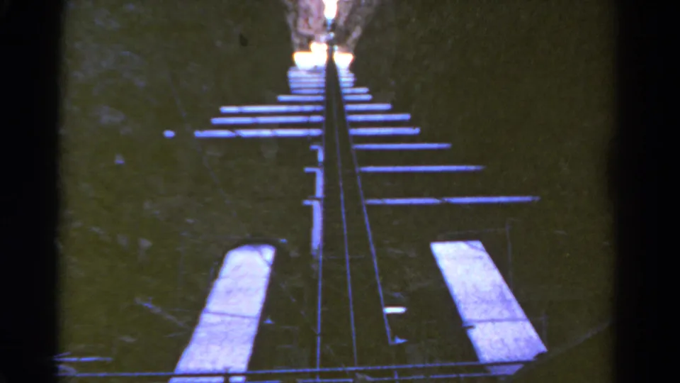 Blue-shifted 1967 Colorado 8mm frame showing the roller coaster rails rising through a narrow canyon-like route.
