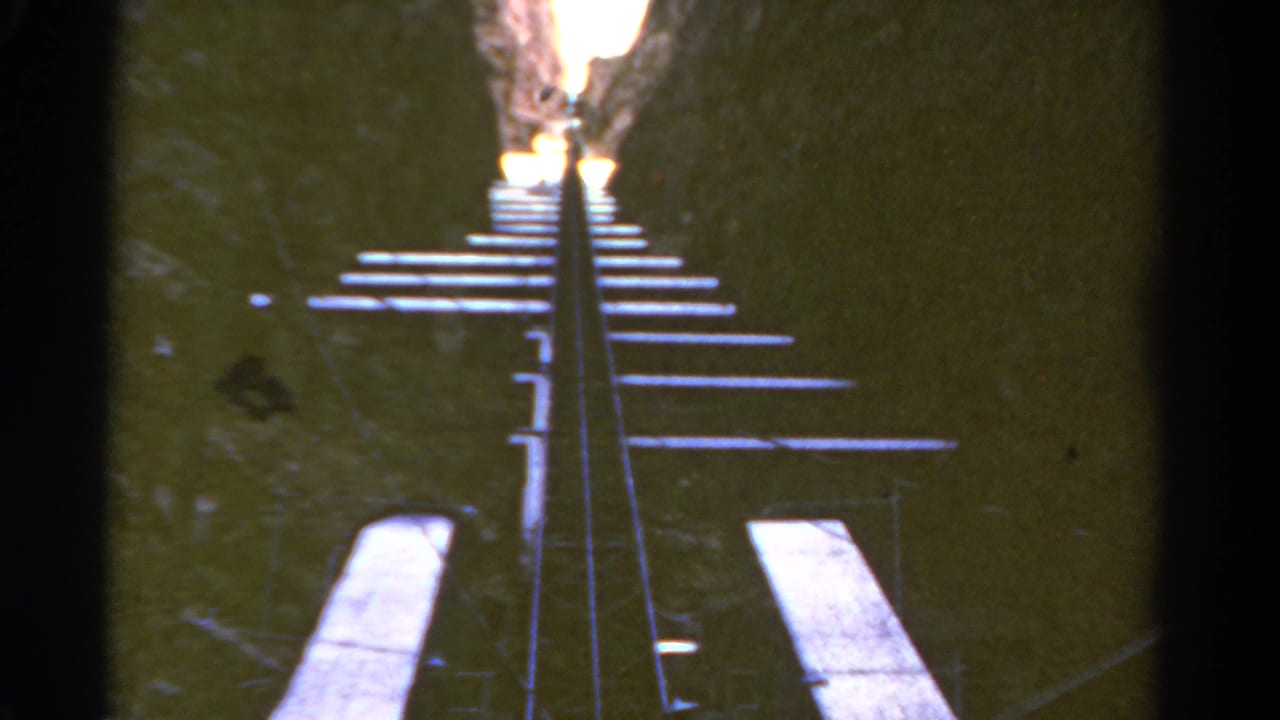 Narrow rail track rising through a dark rocky canyon toward bright light.