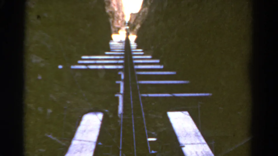 1967 Colorado home-movie frame of rails and cross ties receding toward light in a steep rock passage.