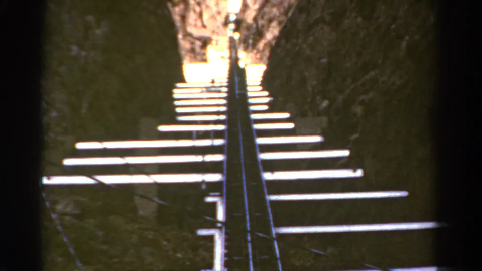 Closer 1967 Colorado 8mm view of a narrow industrial track with bright ties against dark canyon rock.