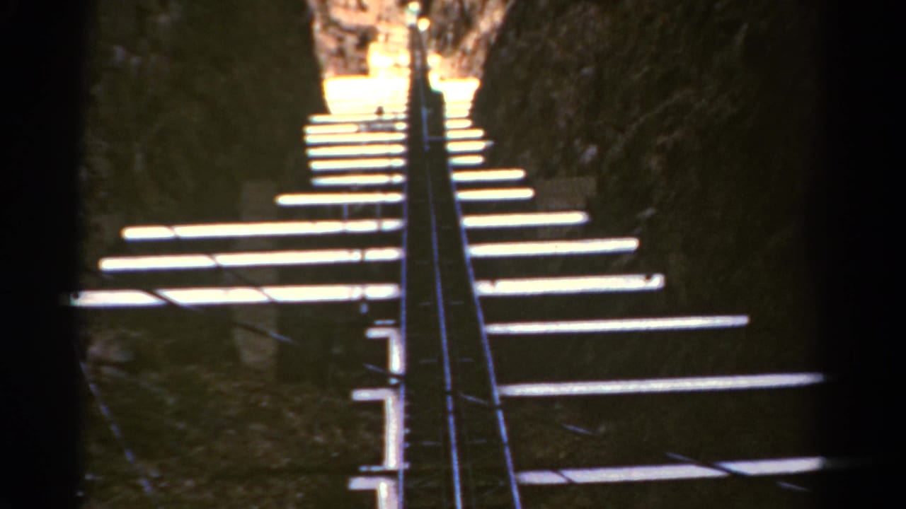 Steep white stair treads climb between dark rock walls toward bright daylight.