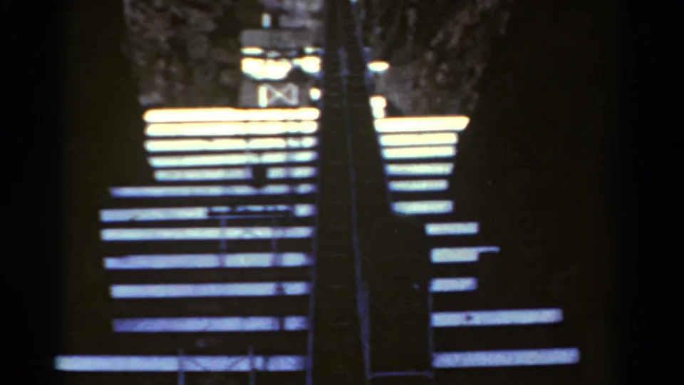 Closer 8mm frame of the Colorado cavern stairway, showing pale steps, dark metal railings, and rough rock walls in high contrast.