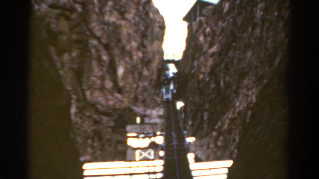 1967 Colorado home-movie frame looking up a steep wooden staircase carved between rugged rock faces.