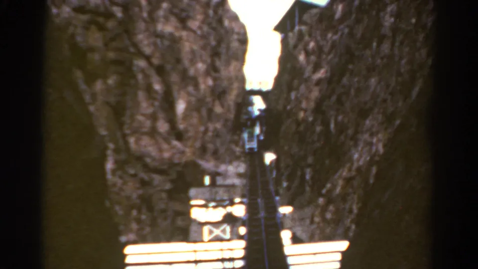 1967 Colorado home-movie frame looking up a steep wooden staircase carved between rugged rock faces.