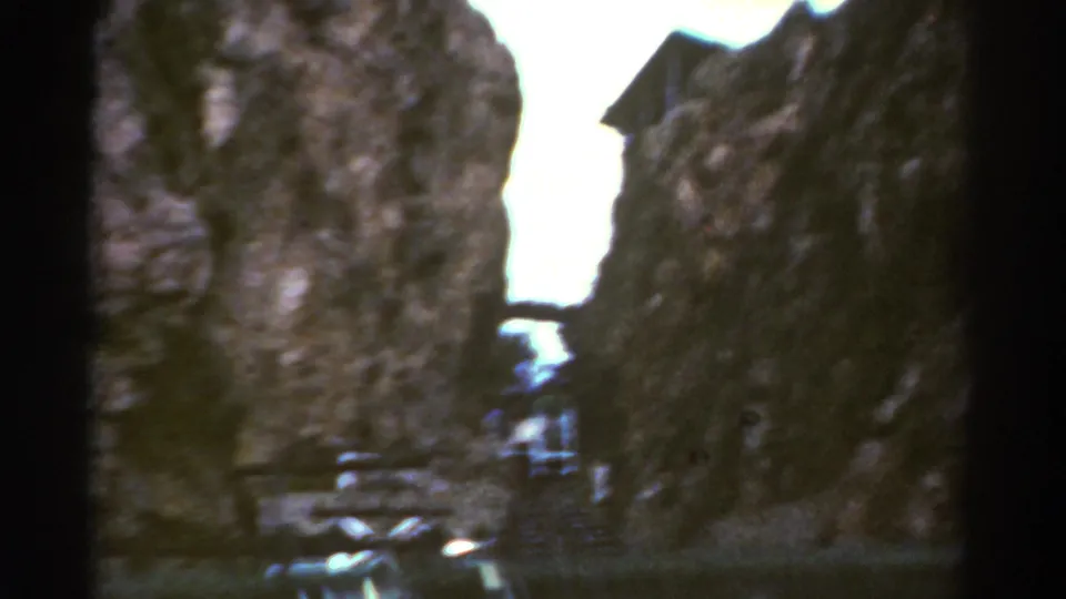 Soft 8mm frame from Colorado in 1967 showing a train partly obscured by shadow as it moves through a rocky canyon.