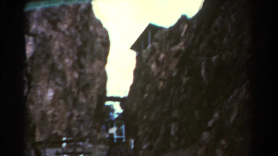 1967 Colorado 8mm frame showing the train farther within a narrow rock canyon, framed by dark film edges and bright sky.