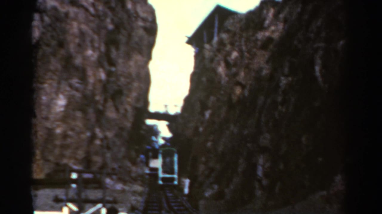 Narrow rocky pass with a small cable car or funicular below a bright opening of sky.