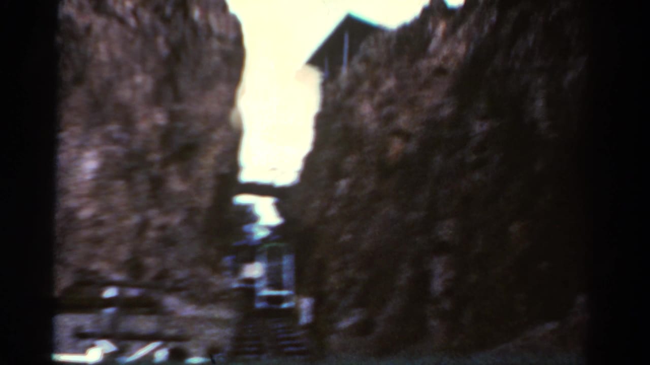 1967 Colorado travel footage frame with a green-and-white cable car or funicular partly visible between tall stone faces.