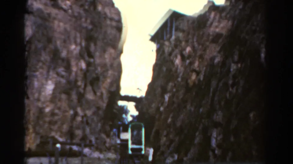 1967 Colorado home-movie frame showing the car low in the rocky passage, with high stone walls on both sides.