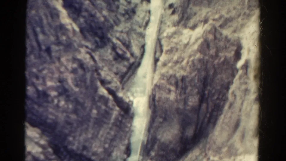 1967 Colorado home-movie frame showing a winding waterway cutting between textured mountain rock faces from an elevated viewpoint.