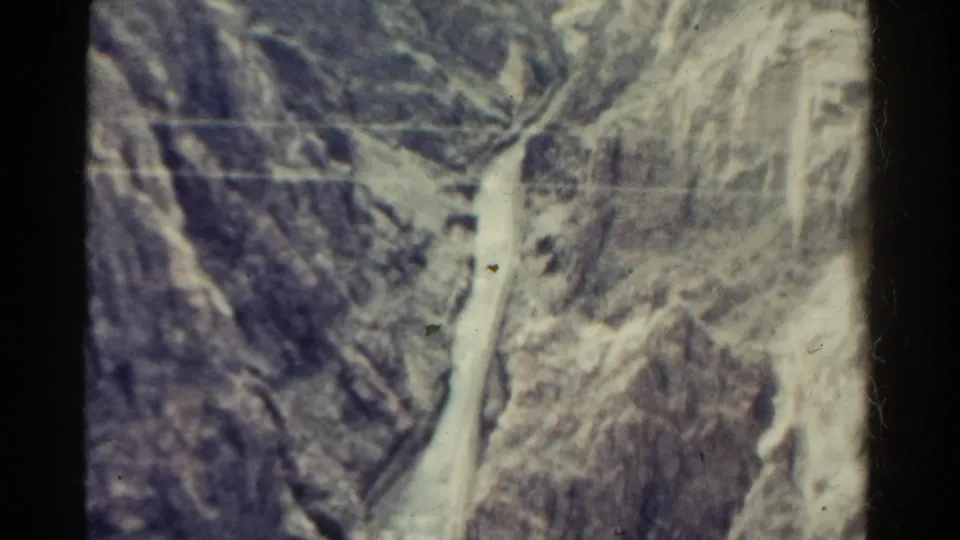 1967 Colorado 8mm frame of a rocky canyon and narrow water channel, with a small distant structure visible near the right side.