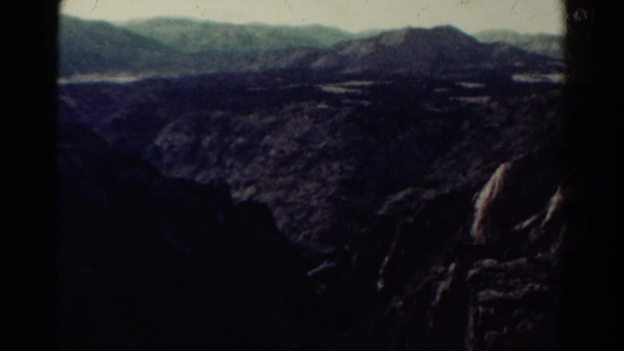 Dark canyon and mountain vista with distant ridges and patches of water or light ground.