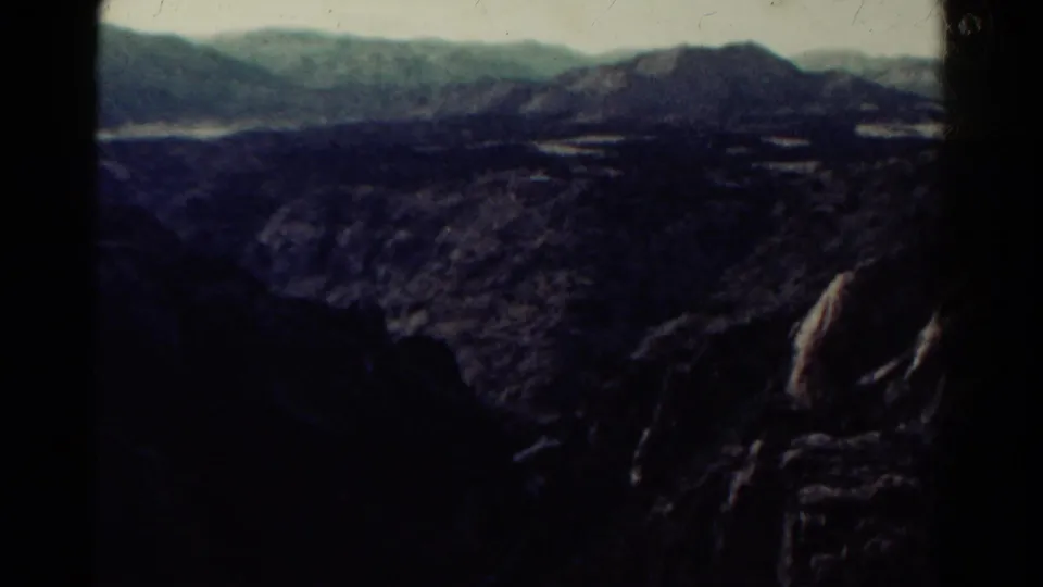 1967 Colorado home-movie view of a dark canyon landscape, distant ridges, and pale patches across the valley floor.