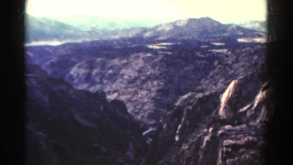 1967 Colorado 8mm frame showing a rugged canyon overlook with dark rocks in front and pale mountains beyond.
