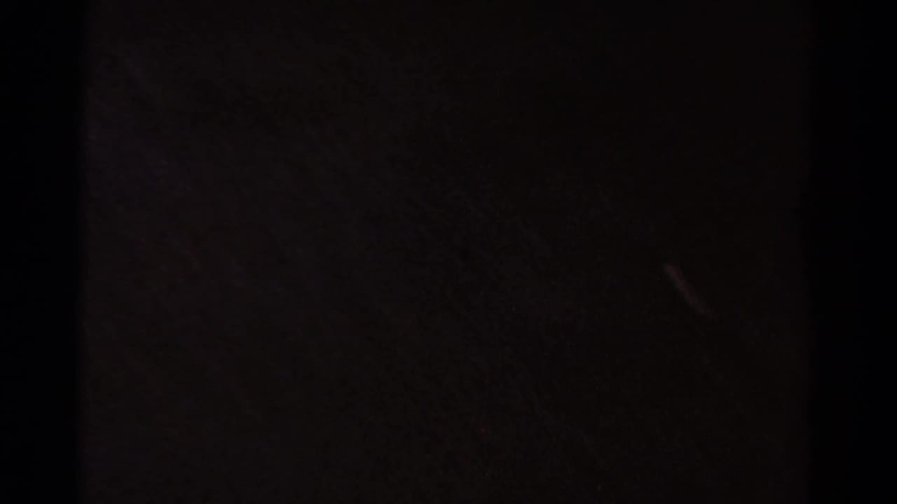 Dark 8mm frame with minimal readable subject detail, likely an underexposed or transitional moment in the clip.