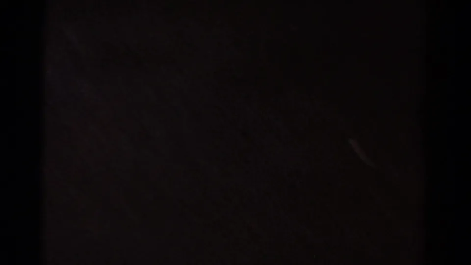 Dark 8mm frame with minimal readable subject detail, likely an underexposed or transitional moment in the clip.