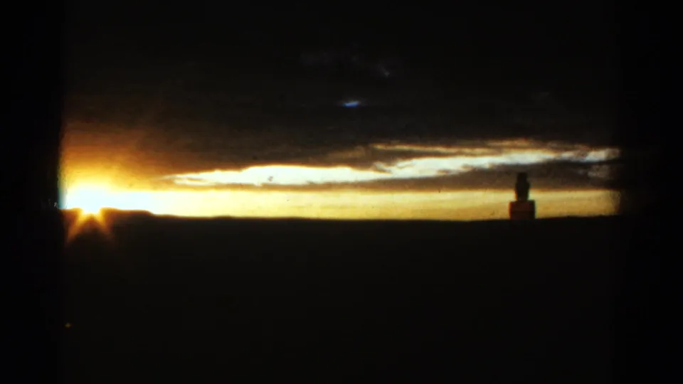 1967 Colorado 8mm frame showing a bright sunset at the horizon with dark foreground silhouettes and layered clouds above.