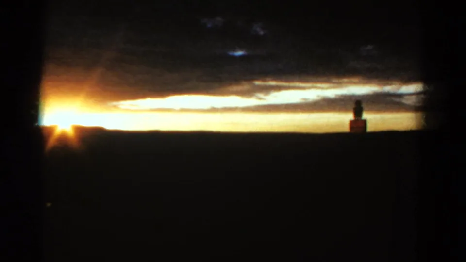 1967 Colorado 8mm frame showing a bright sunset over a dark rural horizon, with clouds and a distant silhouetted figure by a small structure.