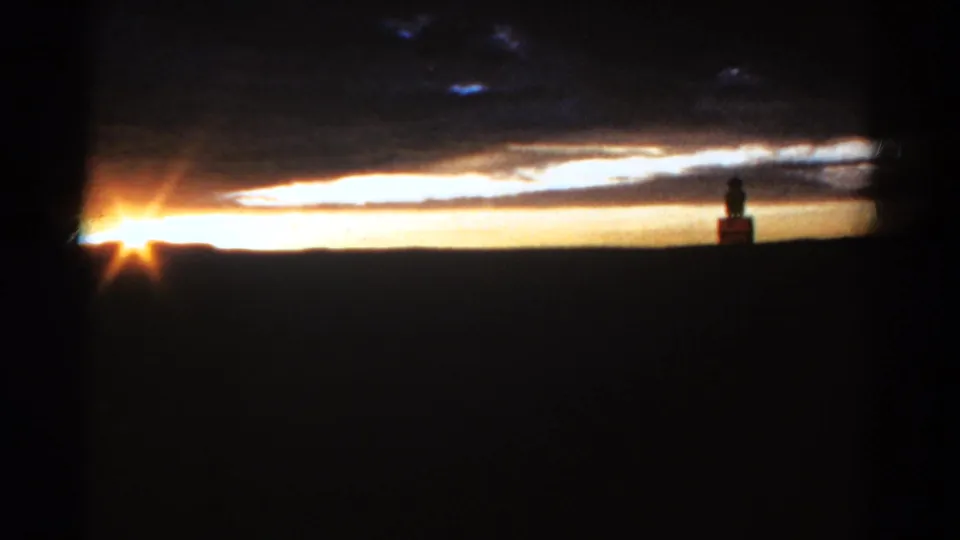 1967 Colorado home-movie frame with the sun near the left edge and a distant statue-like form on the right horizon.