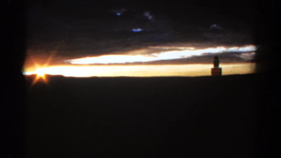 1967 Colorado 8mm sunset frame showing a bright sky band, dark clouds, and a small statue-like silhouette at right.