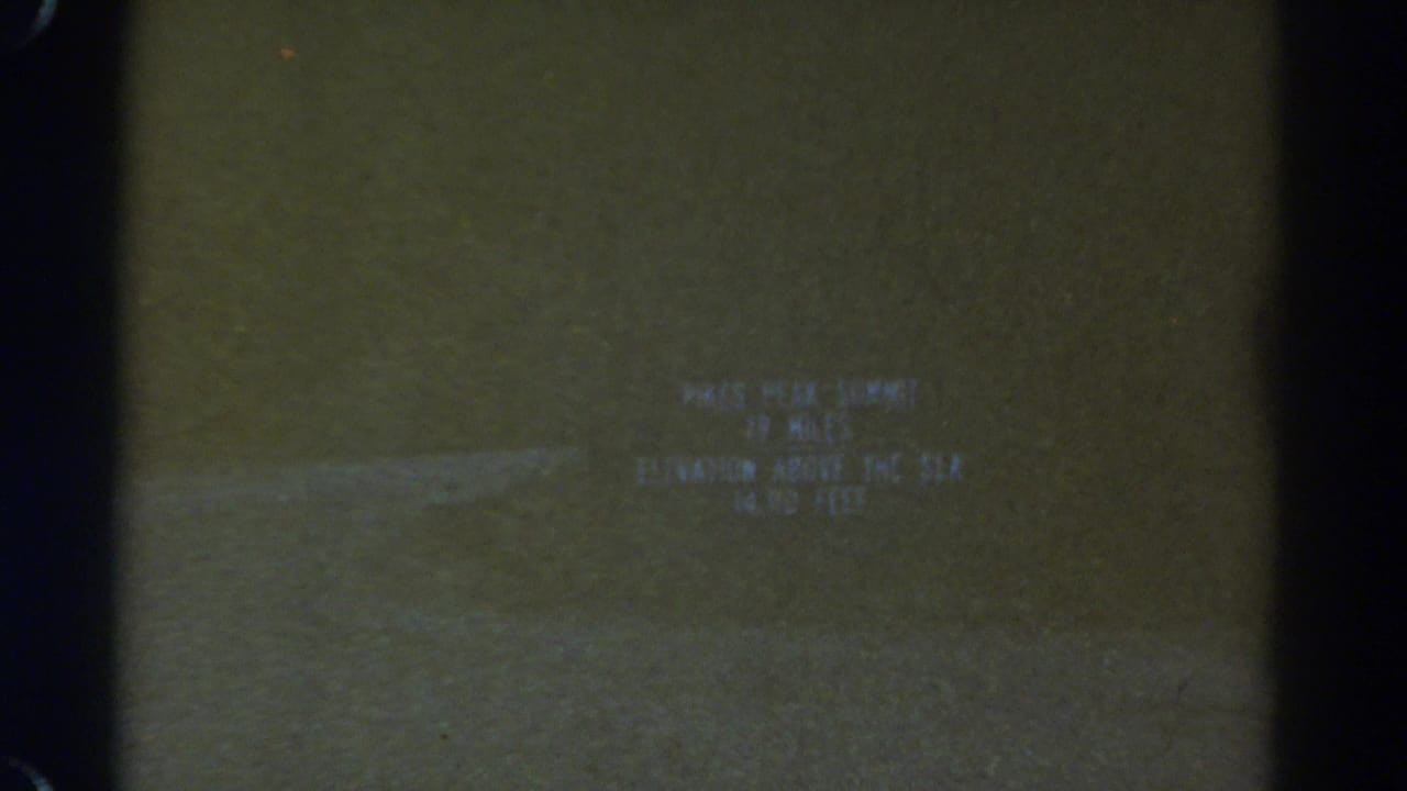 1967 Colorado 8mm frame with a blurred Pikes Peak summit title card and visible film-edge darkness.