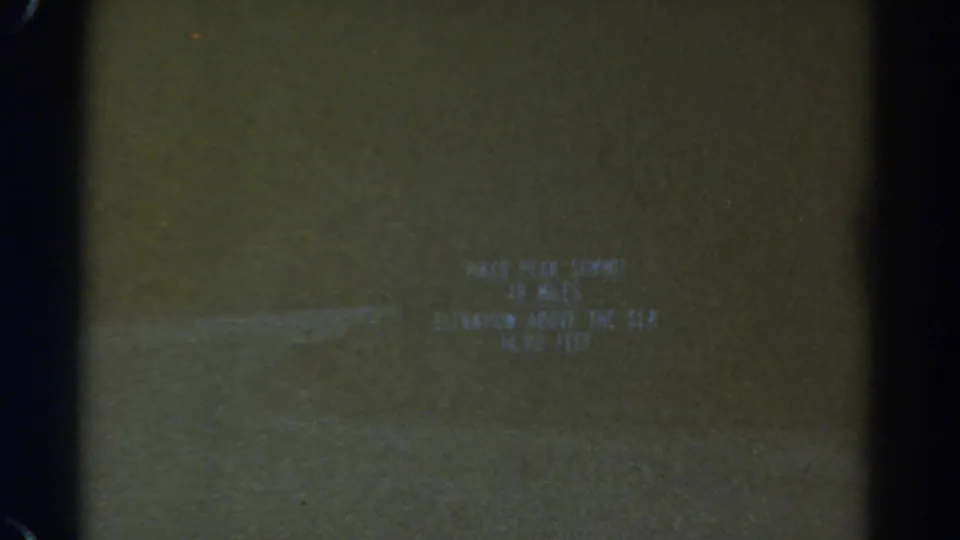 1967 Colorado 8mm frame with a blurred Pikes Peak summit title card and visible film-edge darkness.